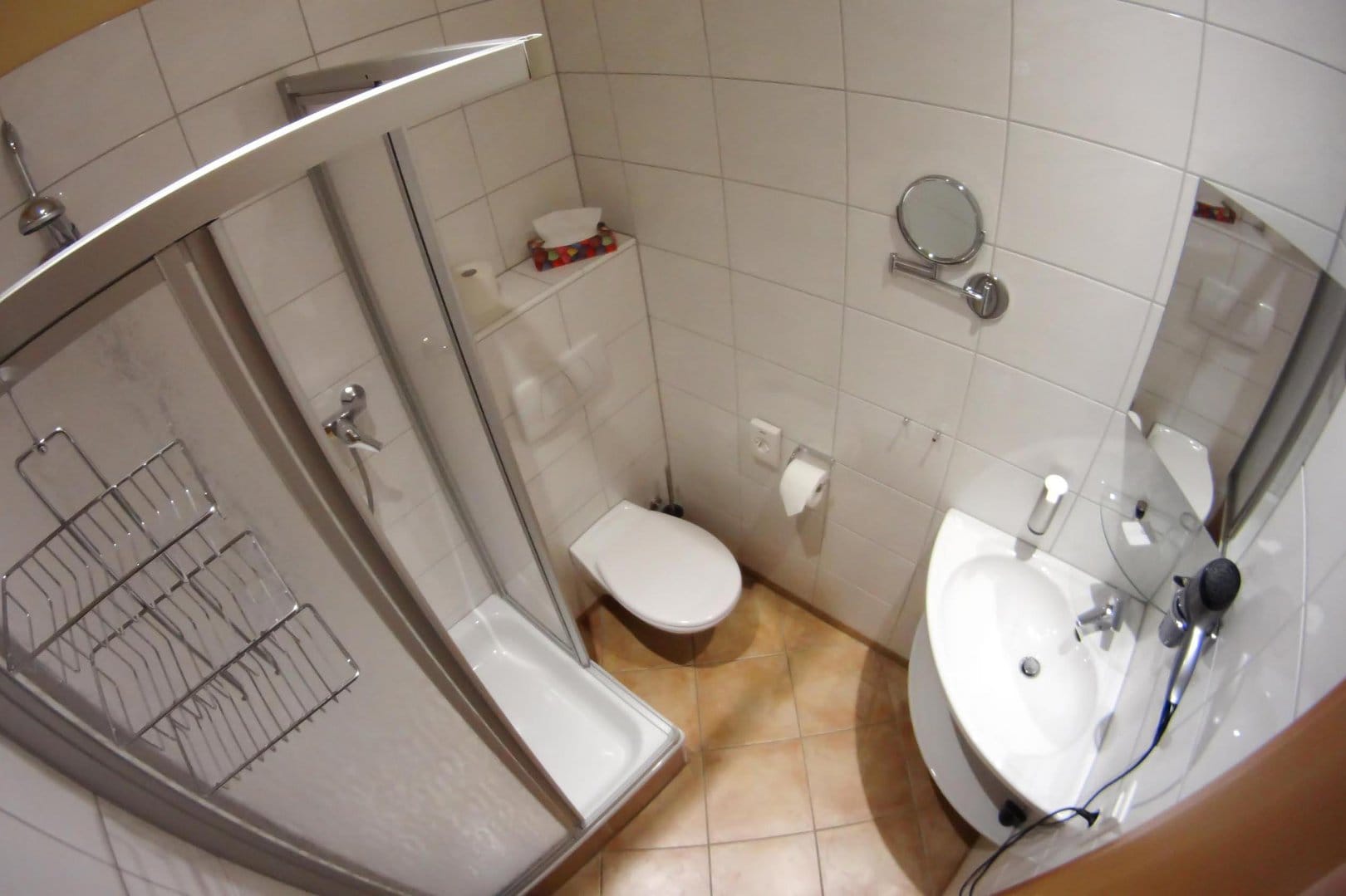 Small, bathroom with white tiles featuring a sink, a shower, a toilet, various mirrors and a hair dryer.