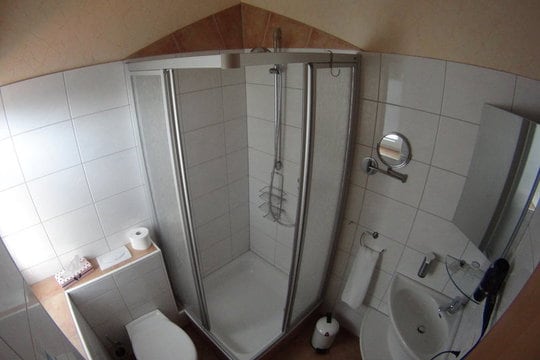 Small, bathroom with white tiles, a sink, a shower, a toilet, various mirrors and a hair dryer.