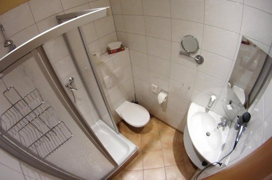 Small, bathroom with white tiles, a sink, a shower, a toilet, various mirrors and a hair dryer.
