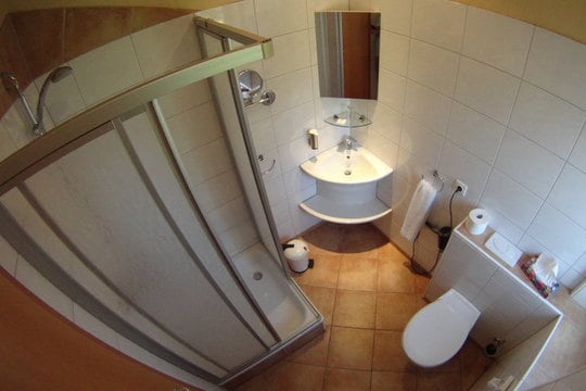 Kleines, weiß gefließtes Badezimmer mit Waschbecken, Duschkabine, Toilette, Spiegeln und Fön.