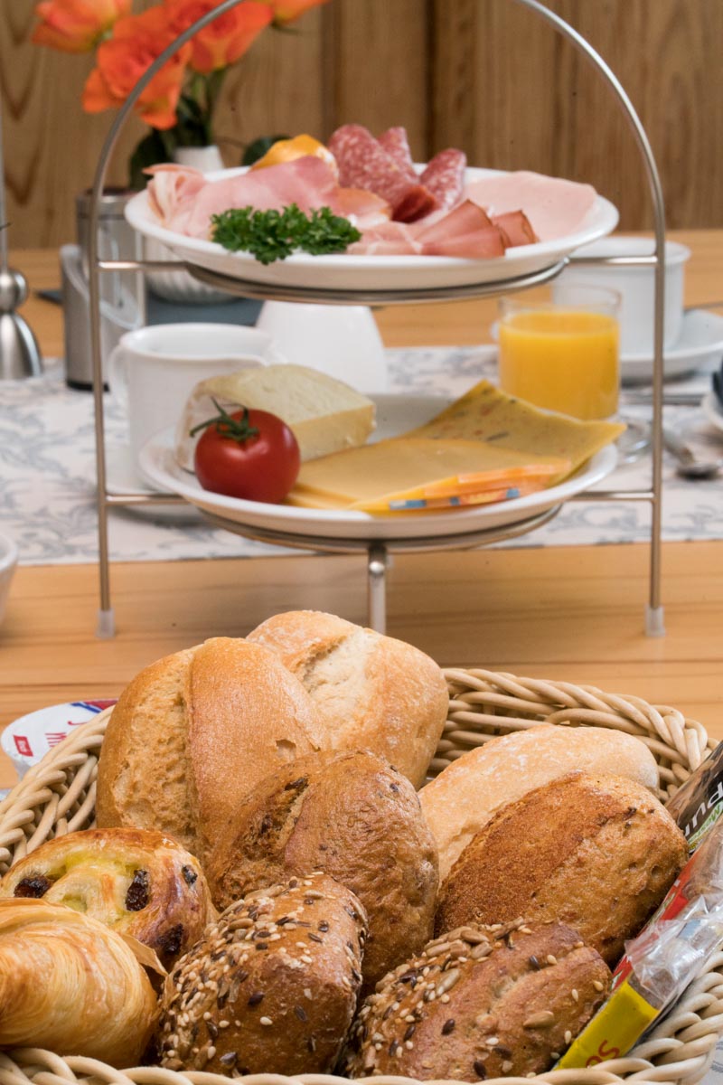 A basked of breads and an etagere with a meat- and cheese-selection, set on a breakfast table.